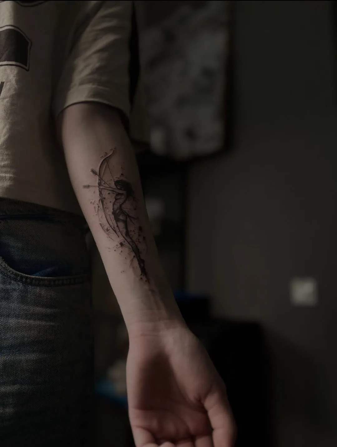 Loka šāvēja silueta tetovējums ar tuša šļakatām apakšdelmā